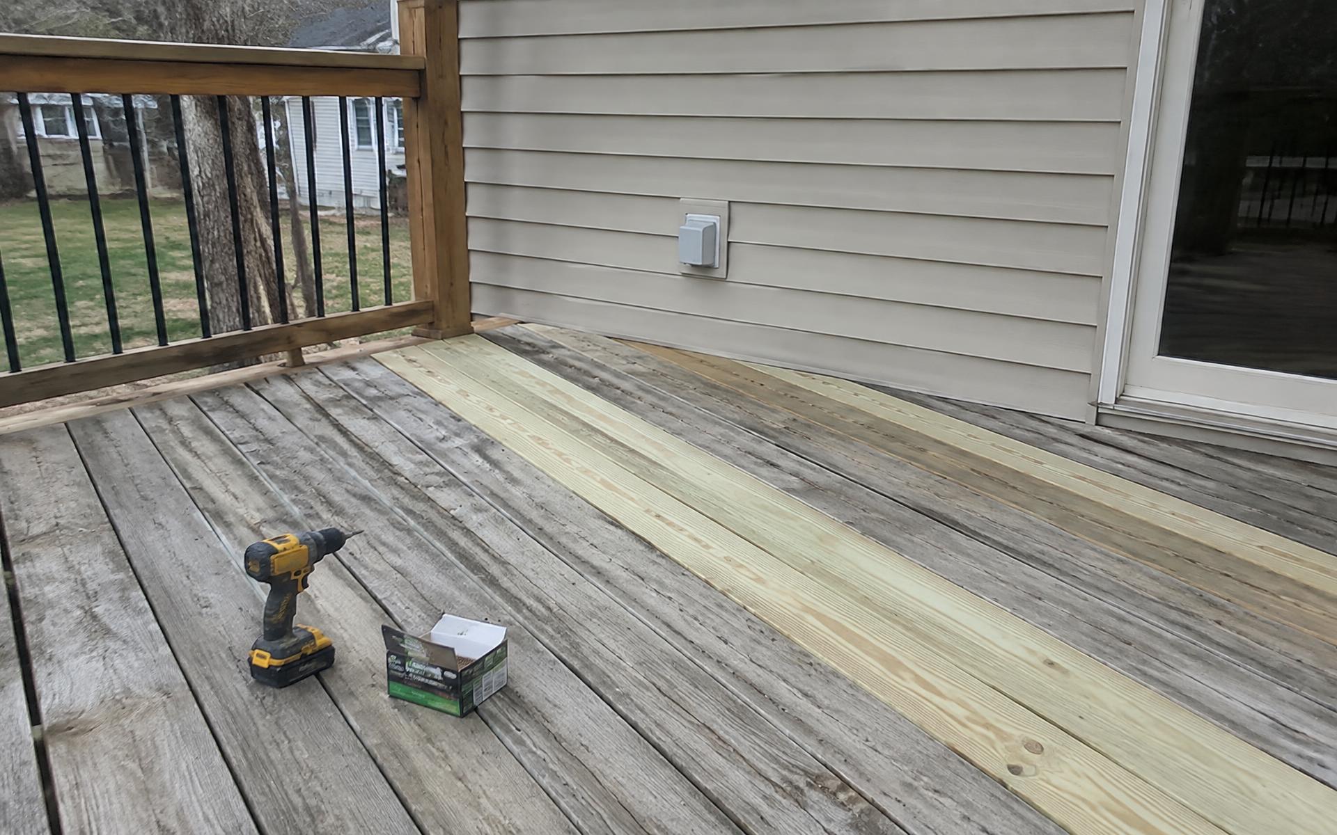 Deck with new boards installed among weathered ones, drill resting nearby